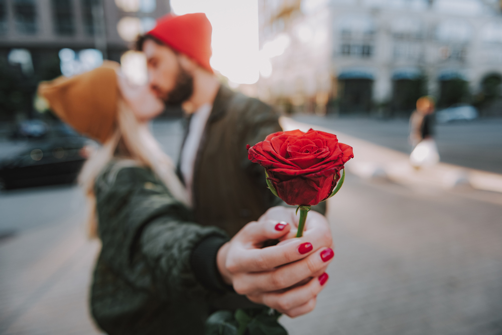 Close up of female and male hands holding red rose. Bearded man kissing his charming girlfriend